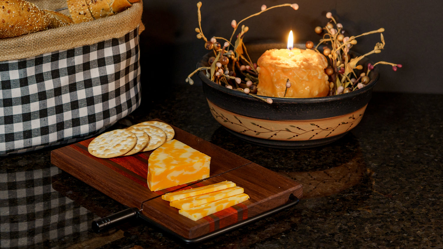 Walnut cheeseboard on a granite countertop with Colby Jack Cheese & crackers lit by candle light.